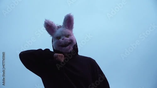scary evil maniac in a rabbit mask looks at the camera and prepares to kill. a crazy man stands in the forest and is illuminated by police flashers. arrest of the killer