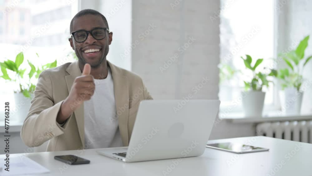 African Man Showing Thumbs Up Sign While using Laptop in Office African Man Showing Thumbs Up Sign While using Laptop in Office