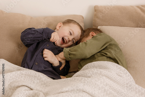 Two little and cute caucasian boys playing together on the bed at home. Interior and clothes in natural earth colors. Cozy environment. Children having fun, two brothers kittle each other. photo