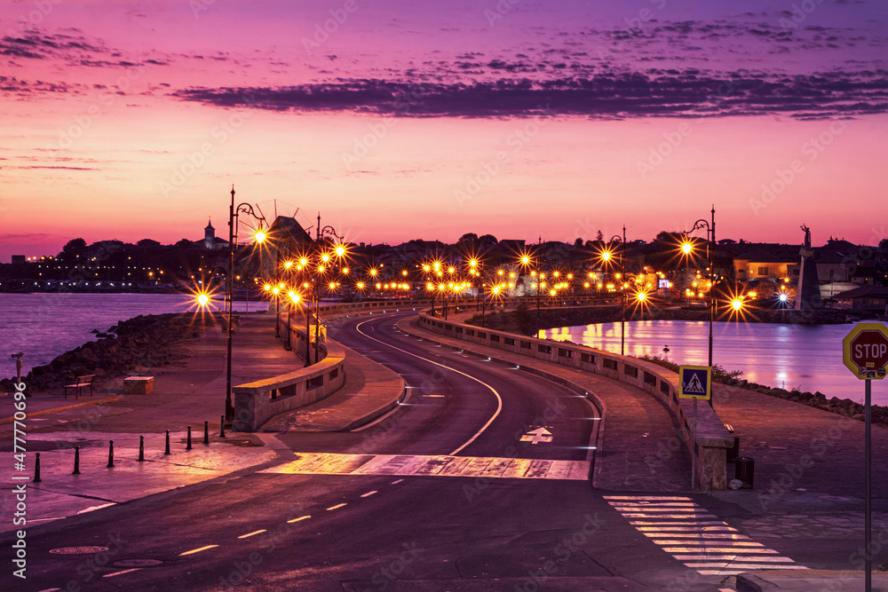 Evening city landscape - view of the road with street lights and the wooden windmill before the entrance to the Old Town of Nessebar, on the Black Sea coast of Bulgaria