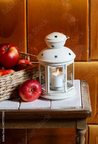 A lantern with candle and basket of apples on the table.