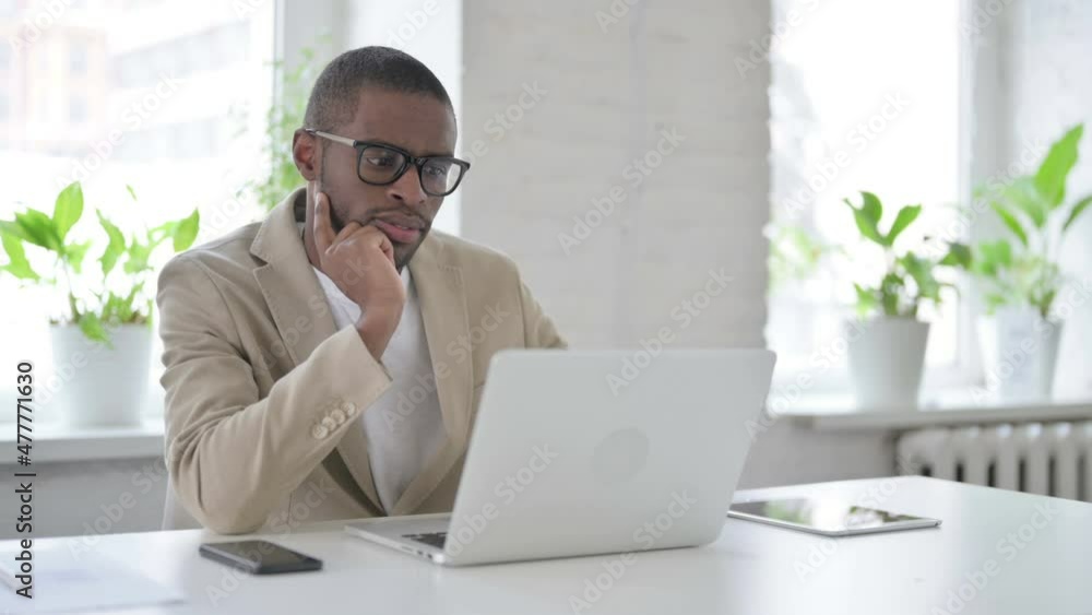 African Man Thinking while Working on Laptop in Office African Man Thinking while Working on Laptop in Office