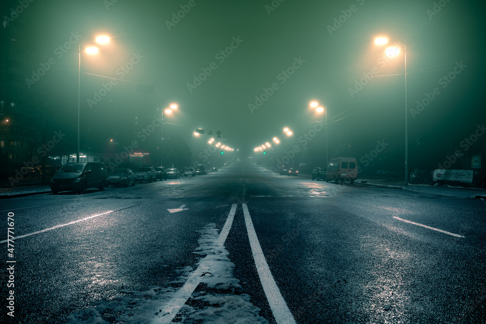 Empty road illuminated by lanterns on a foggy night