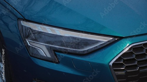 beautiful blue car with glowing headlights. the car enthusiast turns on the headlights at night. winter evening with snow