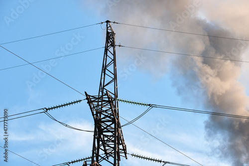 High voltage electric pylons against coal power plant high pipes with black smoke moving upwards polluting atmosphere. Production of electrical energy with fossil fuel concept