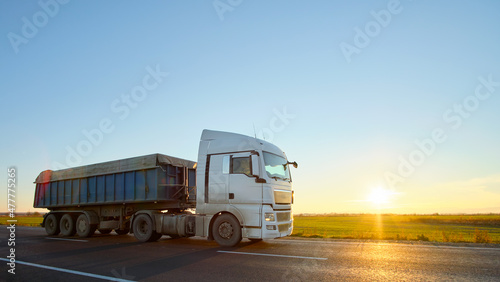 Semi-truck with tipping cargo trailer transporting sand from quarry driving on highway hauling goods in evening. Delivery transportation and logistics concept