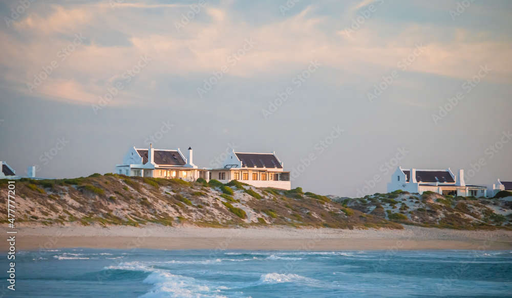Wide shot of holiday homes on beach front at sunset with crashing waves in the foreground in Jacobsbaai, South Africa.