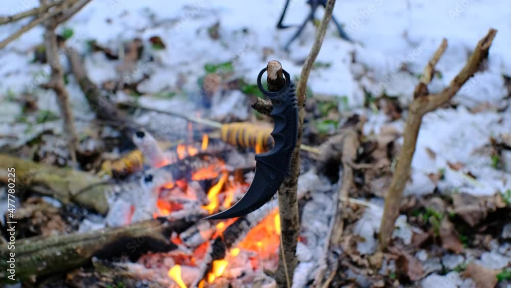 karambit knife on the branch in front of bonfire in the dark snowy forest karambit knife on the branch in front of bonfire in the dark snowy forest