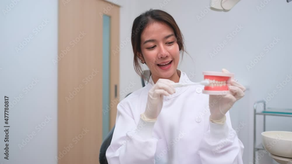 Beautiful Asian dentist use tooth model to explain good way to take care dental health and brush teeth. She present in front of camera look like online teaching for patient or other people. Beautiful Asian dentist use tooth model to explain good way to take care dental health and brush teeth. She present in front of camera look like online teaching for patient or other people.