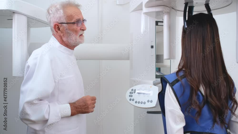 Senior Caucasian dentist control X-ray machine to analysis oral health of Asian woman patient in process of diagnosis for treatment in clinic. Senior Caucasian dentist control X-ray machine to analysis oral health of Asian woman patient in process of diagnosis for treatment in clinic.