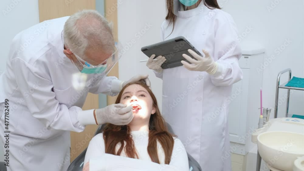 Senior Caucasian dentist stand and do process to check oral health of young girl in clinic and they use many tools and equipment in diagnosis and treatment. Senior Caucasian dentist stand and do process to check oral health of young girl in clinic and they use many tools and equipment in diagnosis and treatment.