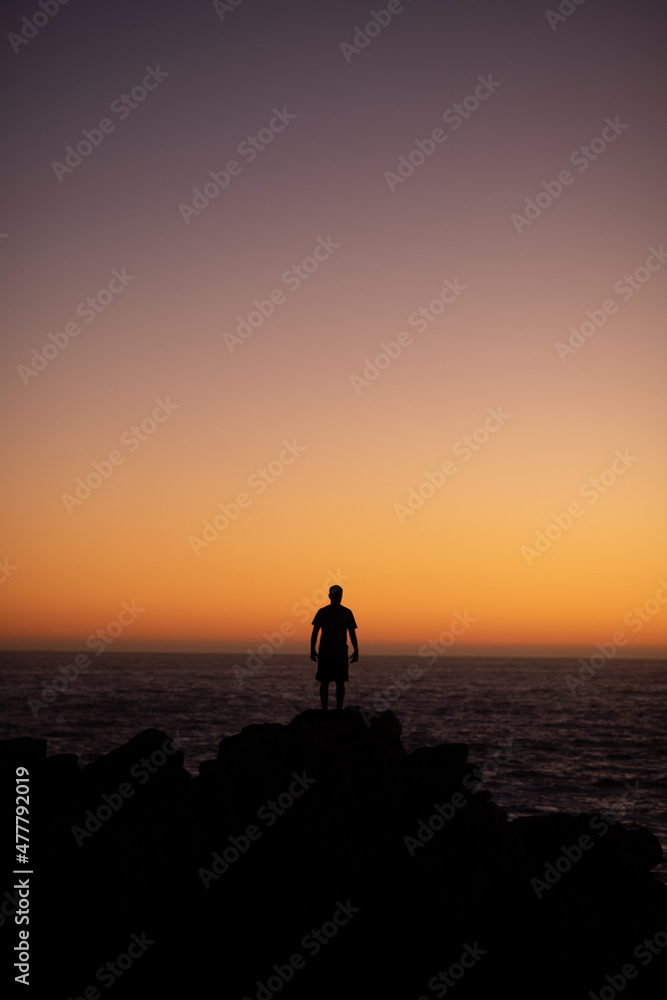 Boy watching the sea water and sunset sky on high rocks on the coast of Concon, Chile.