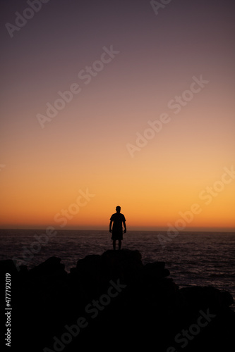 Boy watching the sea water and sunset sky on high rocks on the coast of Concon, Chile.