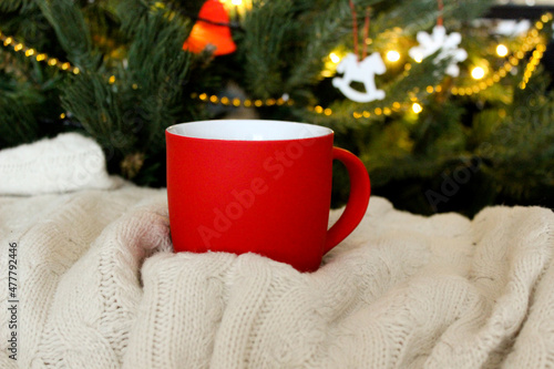 Blank red mug with christmas tree and knitted plaid on background,mat tea or coffee cup with christmas and new year decoration,horizontal mock up with ceramic mug for hot drinks,empty print template.