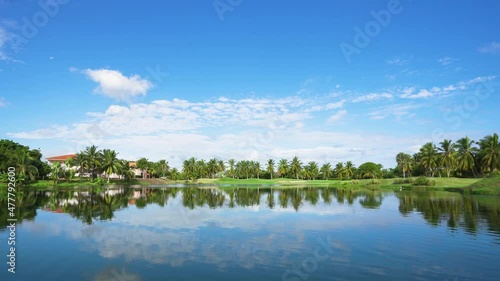 A beautiful lake on a golf course in the Dominican Republic. Green meadow grass background for palms and trees. The blue sky is reflected in the water on a sunny morning. photo