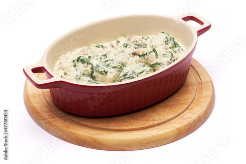 Delicious meatballs with spinach in a creamy sauce in baking dish on white background