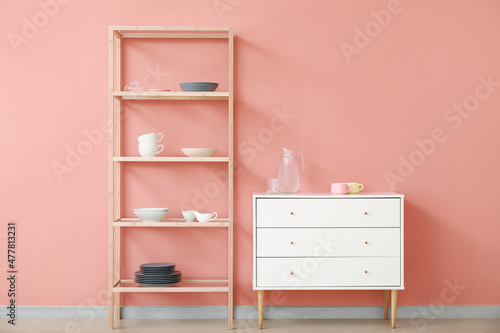 Shelving unit and chest of drawers with dishes near pink wall © Pixel-Shot