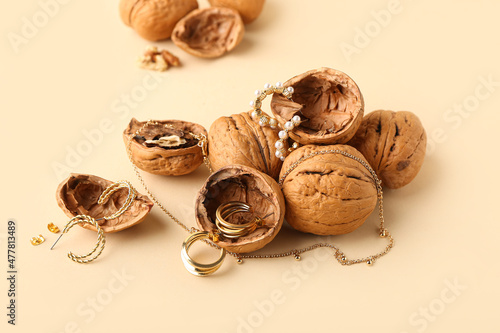 Stylish golden jewelry and walnuts on color background