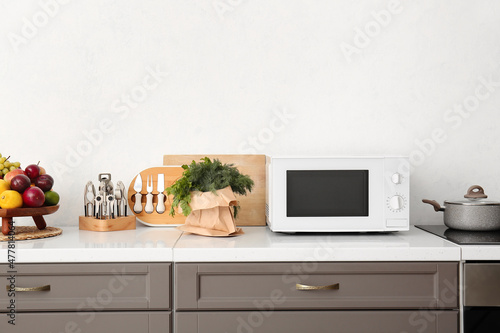 Modern microwave oven, kitchenware and food on counter near light wall