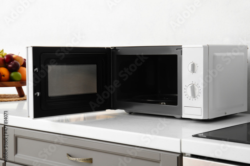Open microwave oven on counter near light wall