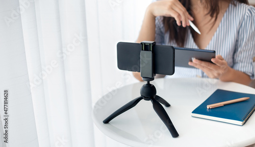 Young asian woman using mobile phone on small tripod live streaming to working or study online, concept working with new normal and social distancing