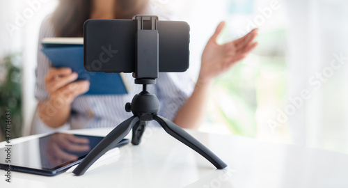Young asian woman using mobile phone on small tripod live streaming to working or study online, concept working with new normal and social distancing