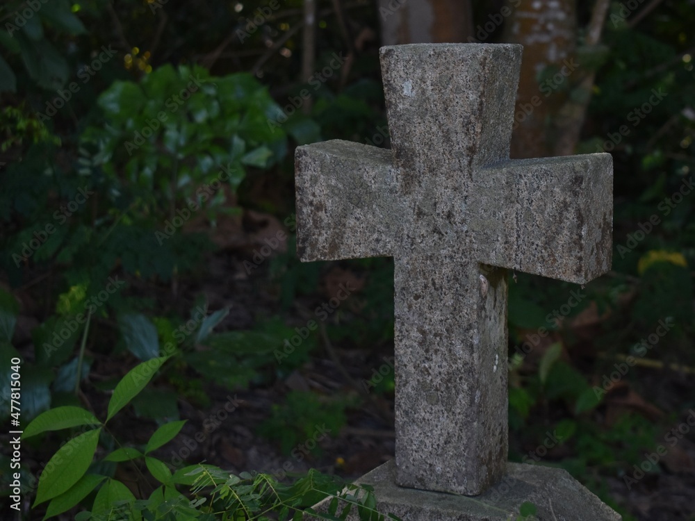Small traditional stone cross on a grave in the forest