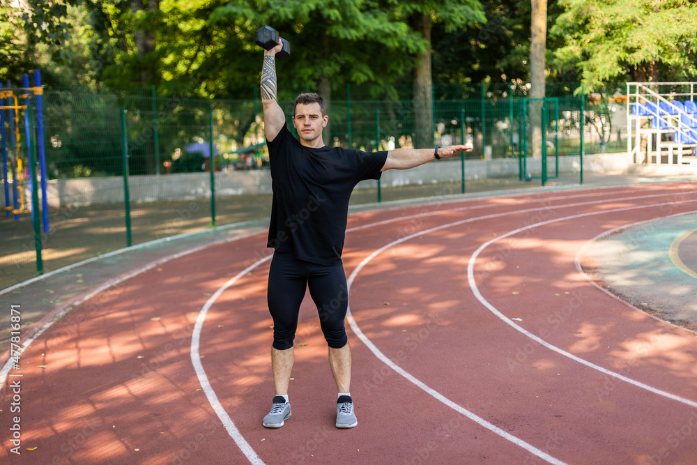 Athletic male training with one dumbbell on stadium Athletic male training with one dumbbell on stadium