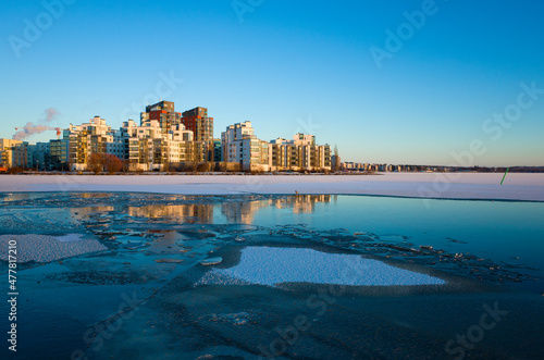 Winter day in Scandinavia, Lakeside residential complex skyline illuminated by low winter sun, Floating ice of frozen lake Malaren, View of residential area Lillaudden, Vasteras, Sweden