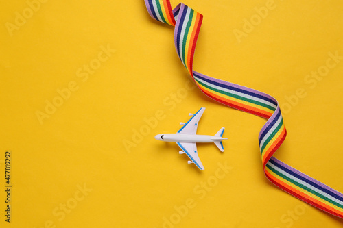Toy passenger plane with lgbt rainbow ribbon on yellow background