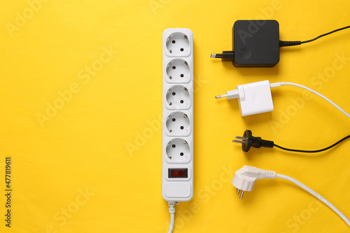 Electrical Extension cord with different plugs and adapters on yellow background. Top view.