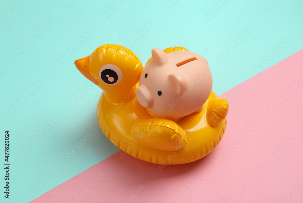 Inflatable duck with piggy bank on pink blue background. Minimal summer concept. Inflatable duck with piggy bank on pink blue background. Minimal summer concept.