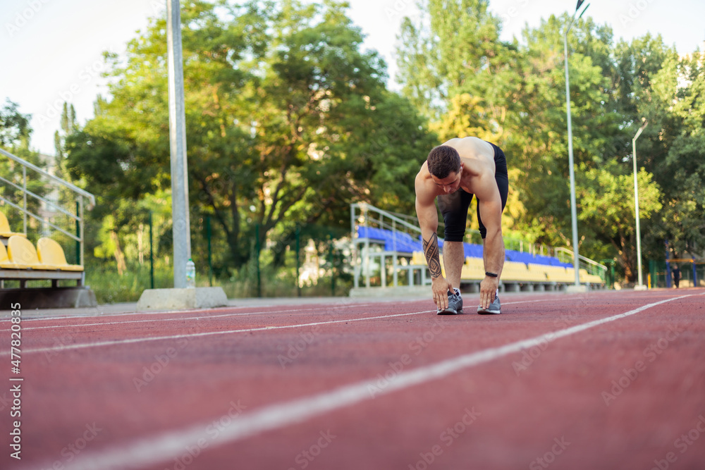 Athletic man with a naked torso practicing stretching exercise before running to the stadium. Healthy lifestyle