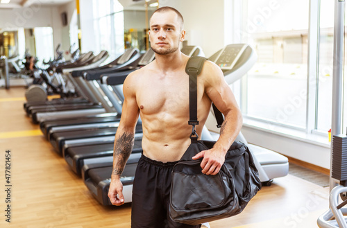 Muscular male athlete with a training bag on his shoulder came to workout in the gym