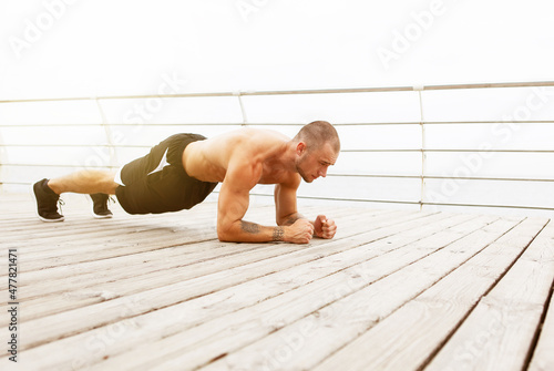 Handsome muscular man with naked torso doing plank exercise on the beach