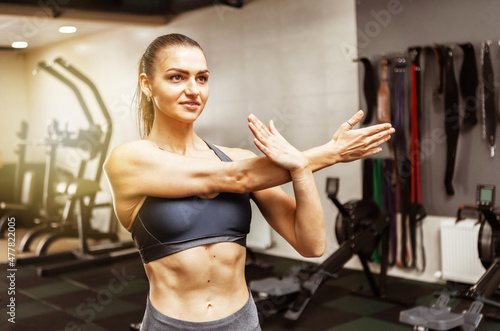 Young fit woman doing stretching hand before intense workout in modern gym
