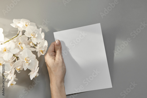 Hands are holding an empty white A5 form on a gray background. Layout top view