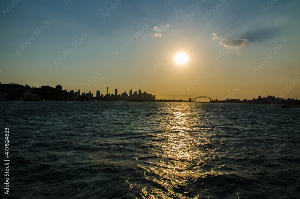 Silhouette sunset at the Harbour with sunlight shining through ocean water and cityscape of Sydney skyscraper.