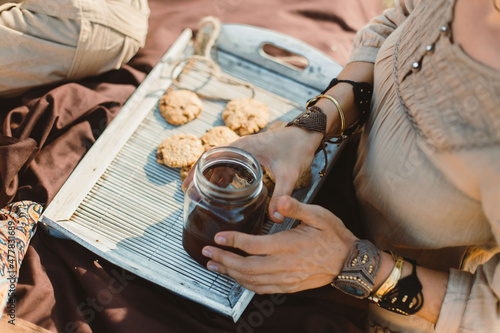 Women's hands are unrecognizable, persons are holding glass Jar with tea. Picnic. Cookies, pleasure, Indian culture. Jewelry, bracelets. Summer autumn.