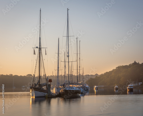 A sunrise scene of the Beaulieu River with sailing boats and pontoon. Misty haze in the background adds to the subtle, peaceful view photo