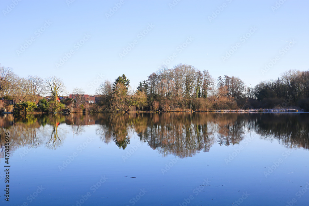 View over lake on bare trees against blue winter sky and waterfront houses - Nettetal (Lobberich), Germany