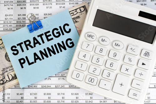 Strategic planning is written on a blue sheet that lies on the financial document. White calculator and dollars. Business and financial concept