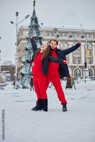 young family guy and girl spend the day in the park on a snowy day. Emotional young couple having fun while walking in the winter city, a lively man hugs his laughing beautiful woman.