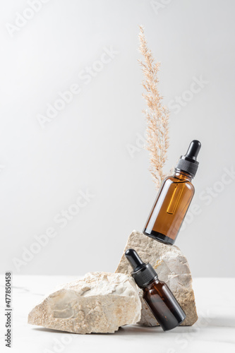 A brown cosmetic bottle with a pipette on astone stand on a gray background, with dried pampas grass behind. Environmental materials. Warm colors. photo