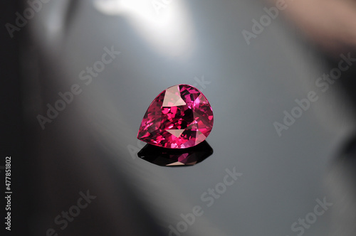 Rhodolite garnet loose gemstone on gray gradient background. Bright raspberry red with pink undertone color beautiful drop shaped garnet stone. Rich deep colorful gem setting. Gemology. Reflection. photo