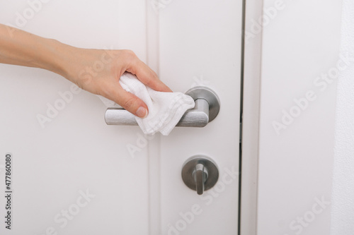 Cleaning black door handles with an antiseptic white wet wipe. Sanitize surfaces prevention in hospital and public spaces against corona virus. Woman hand using towel for cleaning