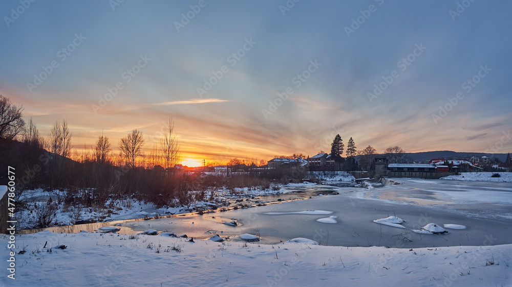Winter evening, sunset over the river. Small dam, hydroelectric power station on an ice-covered river. Winter landscape