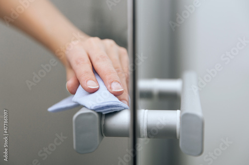 Cleaning glass door handles with an antiseptic wet wipe. Woman hand using towel for cleaning home room door link. Sanitize surfaces prevention in hospital and public spaces against corona virus