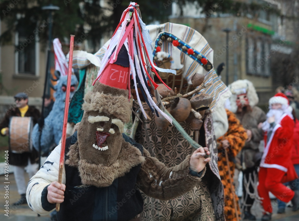 Godech, Bulgaria - January 1, 2022: Mummers in traditional costumes toured the streets of Godech on the first day of 2022. People with a mask called Kukeri dance and perform to scare the evil spirits