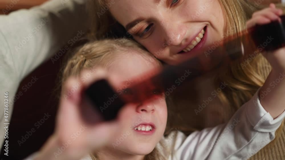 Smiling little child holds processed coloured film roll looking at vintage pictures with parents lying on sofa at home close view slow motion